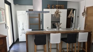 Una cocina moderna con una isla central, taburetes de bar, un refrigerador y una lámpara colgante.
