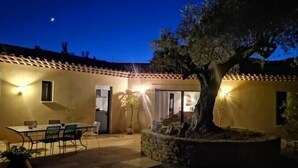 Un edificio con techo de tejas, un comedor con sillas y una mesa, y un sendero de piedra.
