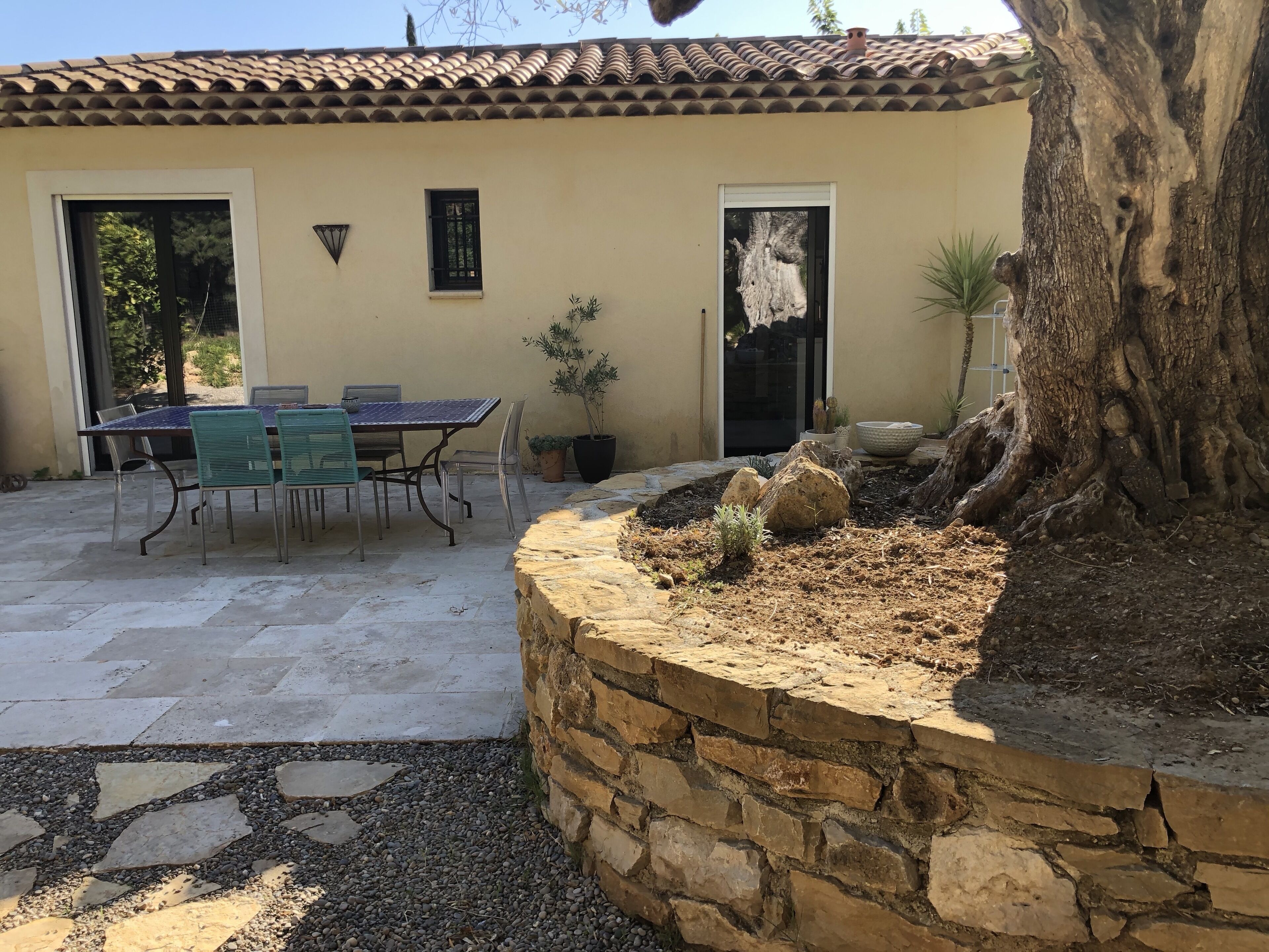 A patio with a table and chairs, a stone wall, and a tree.