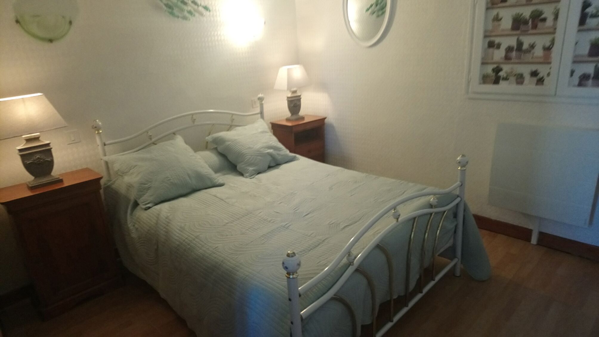 Ein Zimmer mit einem Einzelbett, einem Metallgestell, zwei Nachttischen mit Lampen, einem an der Wand befestigten Regal mit Pflanzen und einem Heizkörper.