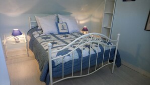 Een net opgemaakt bed met een wit metalen frame, een blauw-witte quilt en twee bedlampjes.