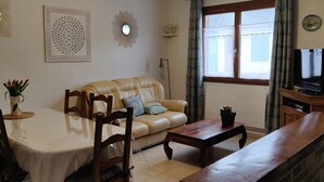 Een woonkamer met een beige bank, een houten salontafel en een eettafel met stoelen.