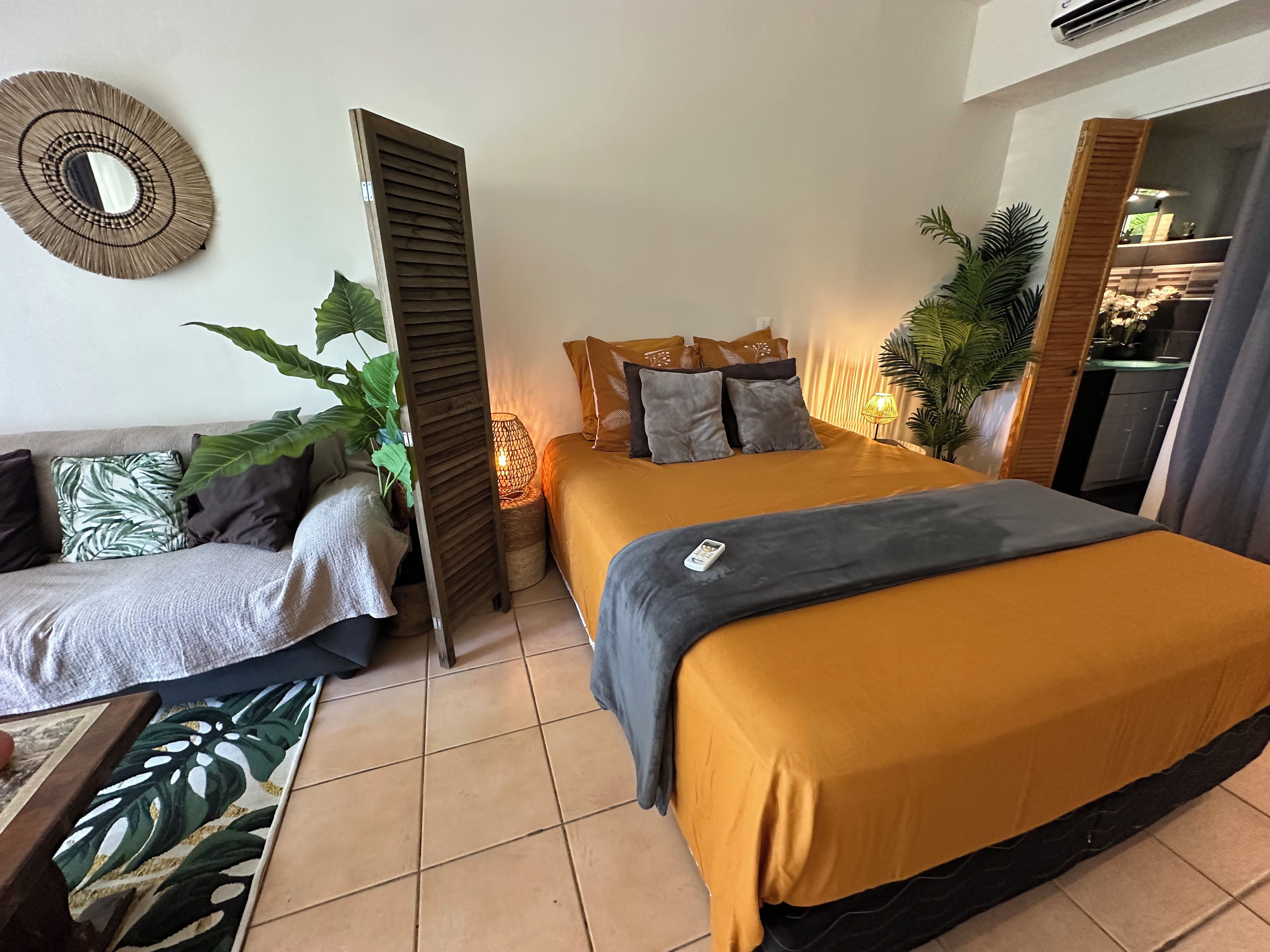 Een slaapkamer met een bed, een bank, een nachtkastje, een lamp en een potplant.