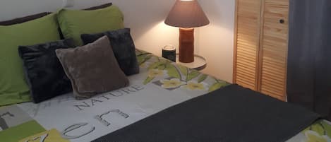 A bedroom with a bed, pillows, a bedside lamp, a magazine, a wardrobe, and an air conditioning unit.