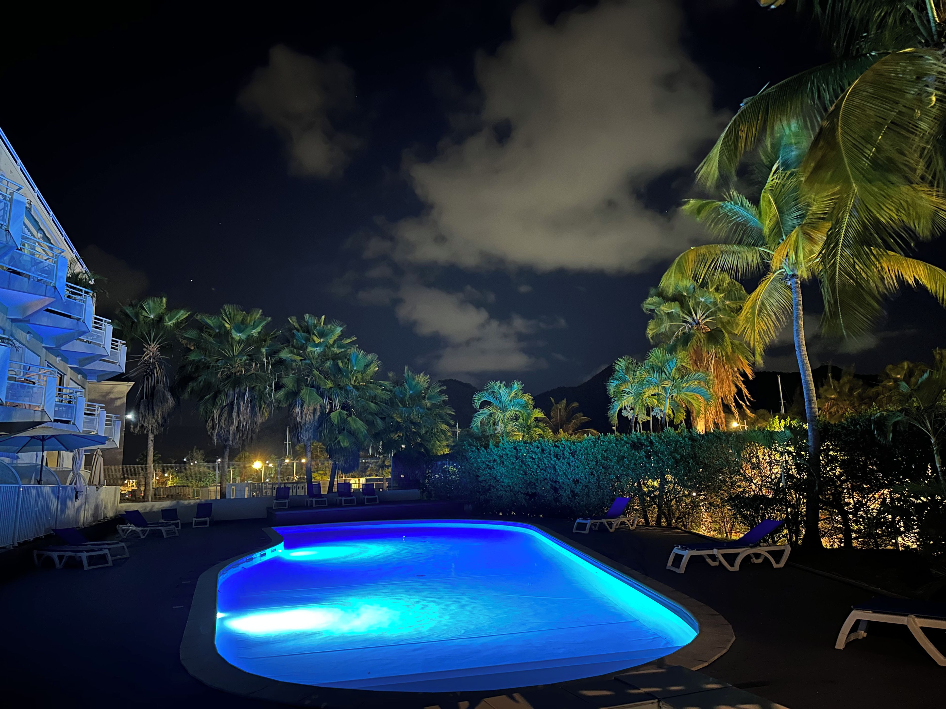 A swimming pool with lounge chairs, palm trees, and a building with balconies.