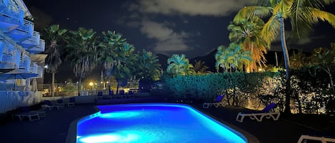 A swimming pool with lounge chairs, palm trees, and a building with balconies.