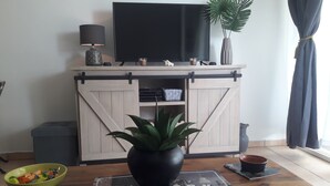 A living room with a TV, a plant, a coffee cup, and a bowl of fruit on a wooden table.