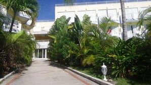 A pathway leading to a building with balconies and a white facade, surrounded by lush tropical vegetation.