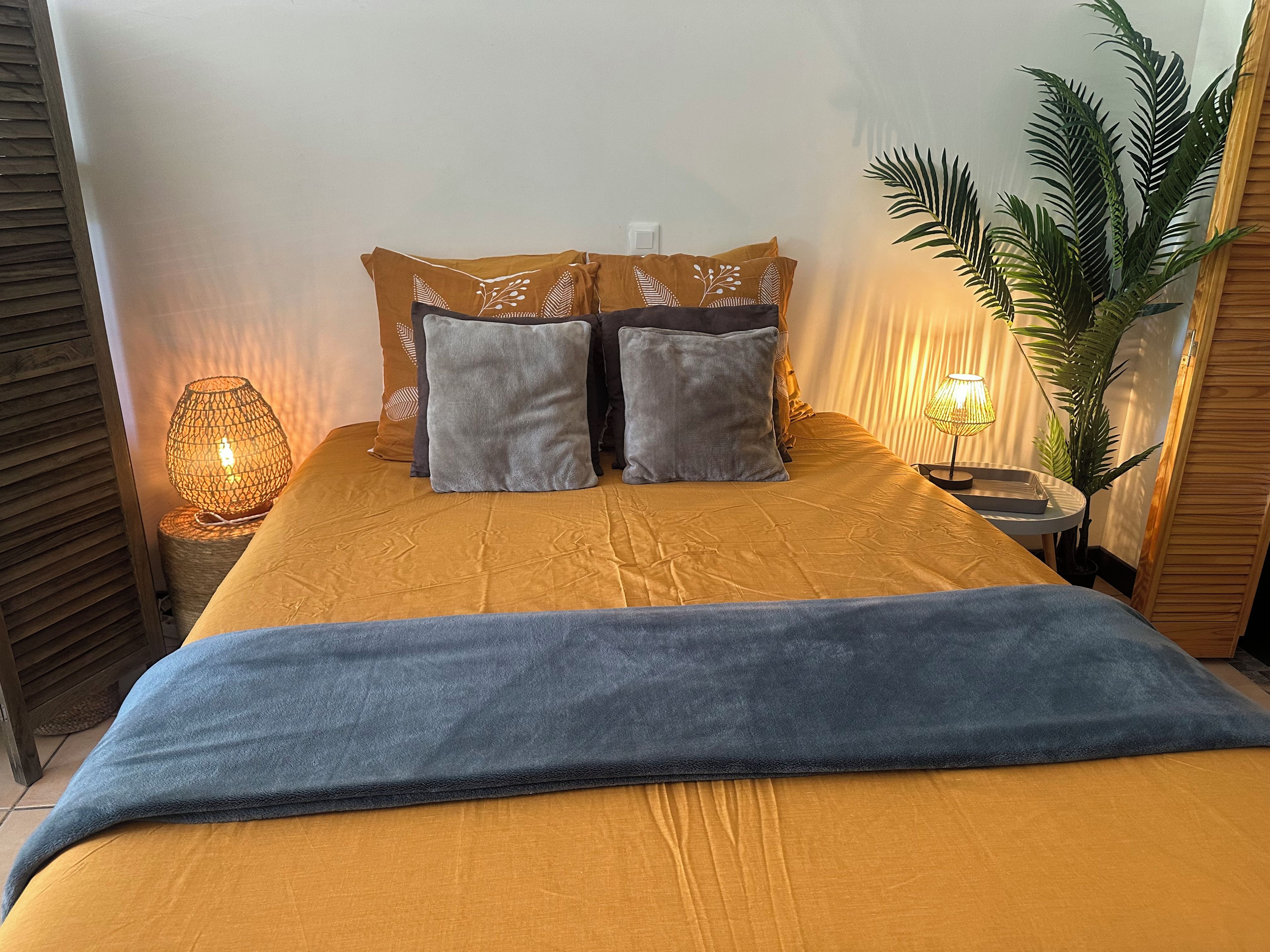 Ein Bett mit einer orangefarbenen, strukturierten Tagesdecke, zwei grauen Kissen und einer blauen Decke.