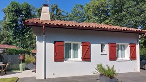 A small, single-story house with a red-tiled roof, white walls, and red shutters. There is a chimney on the roof, and the house is surrounded by a fence and greenery. - Bidart, pretty apartment for 4 people, close to beaches and center of Guéthary  (Bidart)
