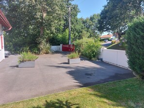 Un'area di parcheggio con un cancello rosso, circondata da vegetazione e una recinzione bianca.