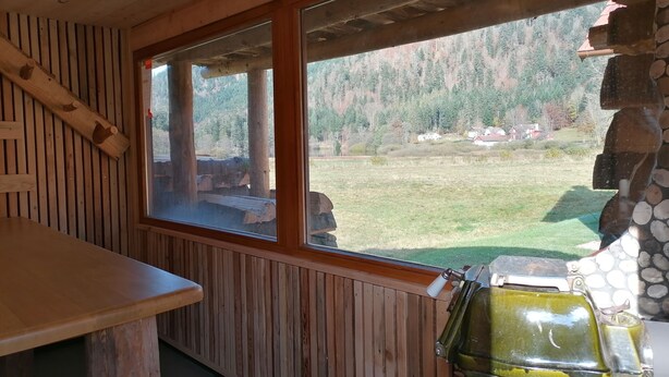 L’intérieur d’un chalet en bois, avec une grande fenêtre donnant sur une zone boisée.