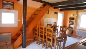 Une cuisine avec un escalier en bois, une table à manger avec des chaises et un sol carrelé.