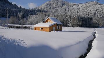 Une cabane en bois dont le toit est recouvert de neige, entourée d’un paysage enneigé et avec une montagne en arrière-plan.