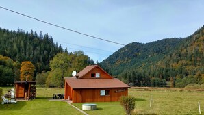 Une cabane en bois avec une antenne parabolique, un petit abri de jardin et une pelouse avec une table et des chaises.