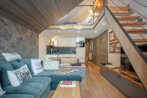 Relax in this open-plan living space with a loft area above the kitchen, featuring a sofa, coffee table, and bookshelf.