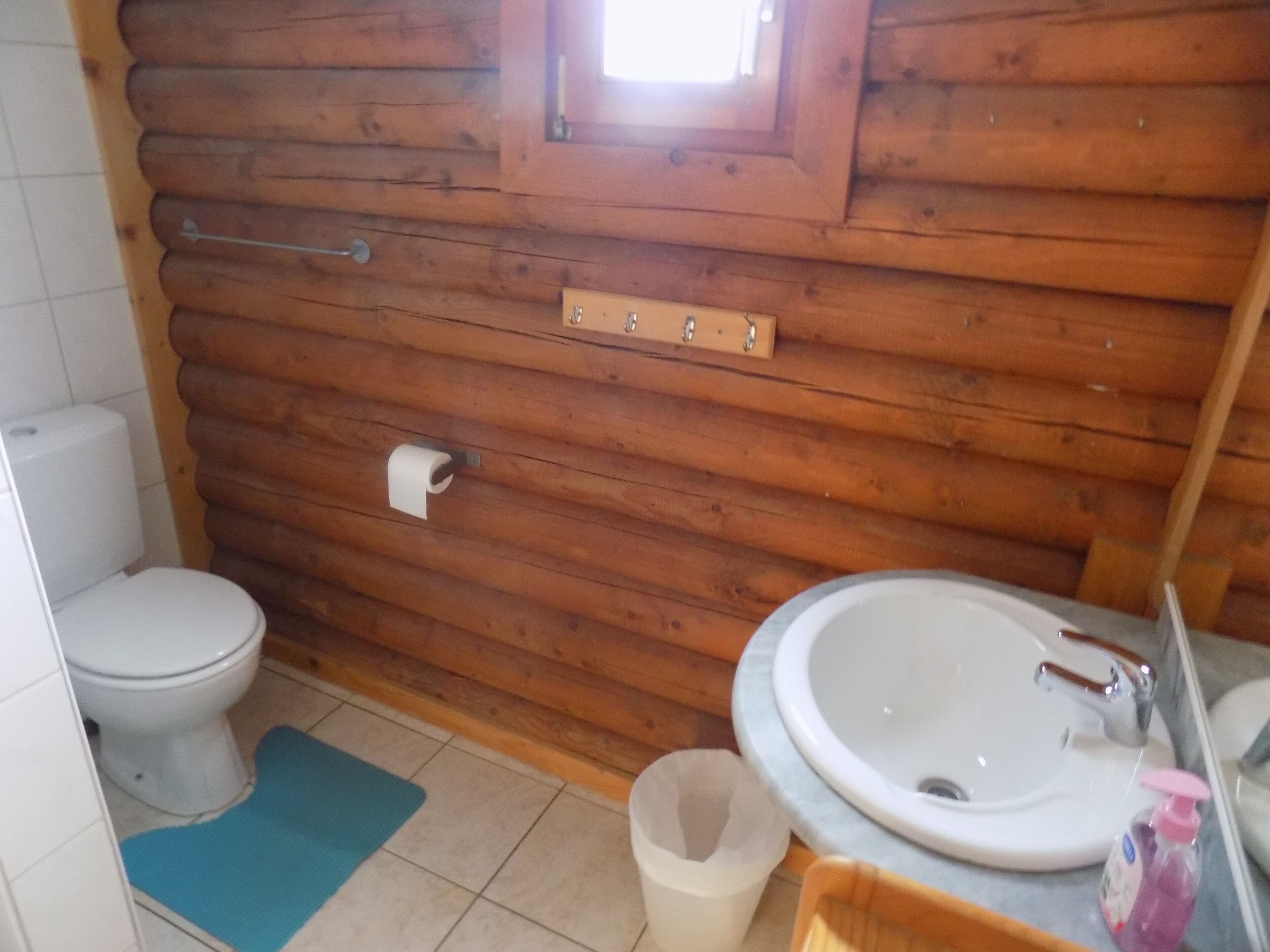 Ein Badezimmer im Holzblockhaus-Stil mit Toilette, Waschbecken und einem Fenster über dem Waschbecken.