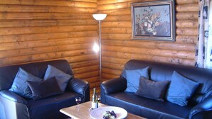 Ein Interieur einer Blockhütte mit zwei Ledersofas, einem Tisch mit Trauben und einer Flasche, sowie einer Stehlampe.