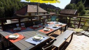 Ein Essbereich im Freien mit einer Holzterrasse, Tischen, die mit Tellern, Gläsern und Besteck gedeckt sind, umgeben von Stühlen.