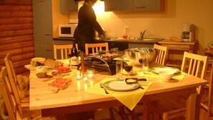 Ein Essbereich mit Holztisch, gedeckt für eine Mahlzeit, eine Person kocht in der Küche und eine Mikrowelle ist über dem Herd angebracht.