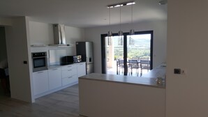 Une cuisine moderne avec des meubles blancs, un four encastré et un four à micro-ondes. Une grande fenêtre offre une vue sur l’extérieur.