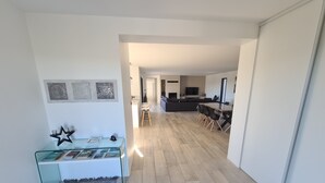 Un espace de vie moderne avec une table basse en verre, un tapis à motifs et un coin repas comprenant une table et des chaises en bois.