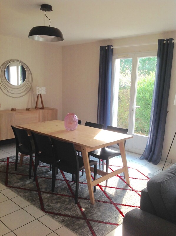 A dining area with a wooden table and chairs, a small cabinet, a mirror, and a view through a glass door to the outside.