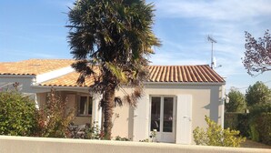 Una casa de un piso con techo de tejas, una palmera y una antena parabólica.