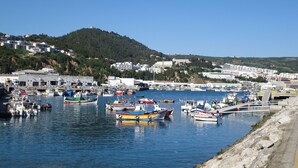 Un puerto con barcos amarrados, una costa rocosa y edificios al fondo.