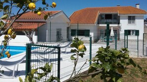 Una casa de dos pisos con piscina, rodeada por una cerca de metal.