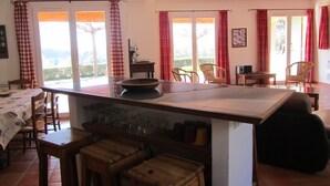 Een keuken met een centraal eiland, houten stoelen, een eettafel en een uitzicht door grote ramen.
