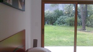 Ein Schlafzimmer mit Bett, einem Bild an der Wand und Blick auf einen Garten durch eine Schiebetür.