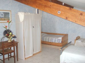 Een kleine, knusse kamer met een houten bed, een tafeltje en een stoel. Aan de zijkant hangt een gordijn en er is een houten balk in het plafond.