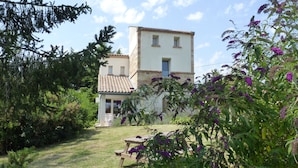 Une maison avec un toit en tuiles, un petit porche et une cour verdoyante avec une table de pique-nique.
