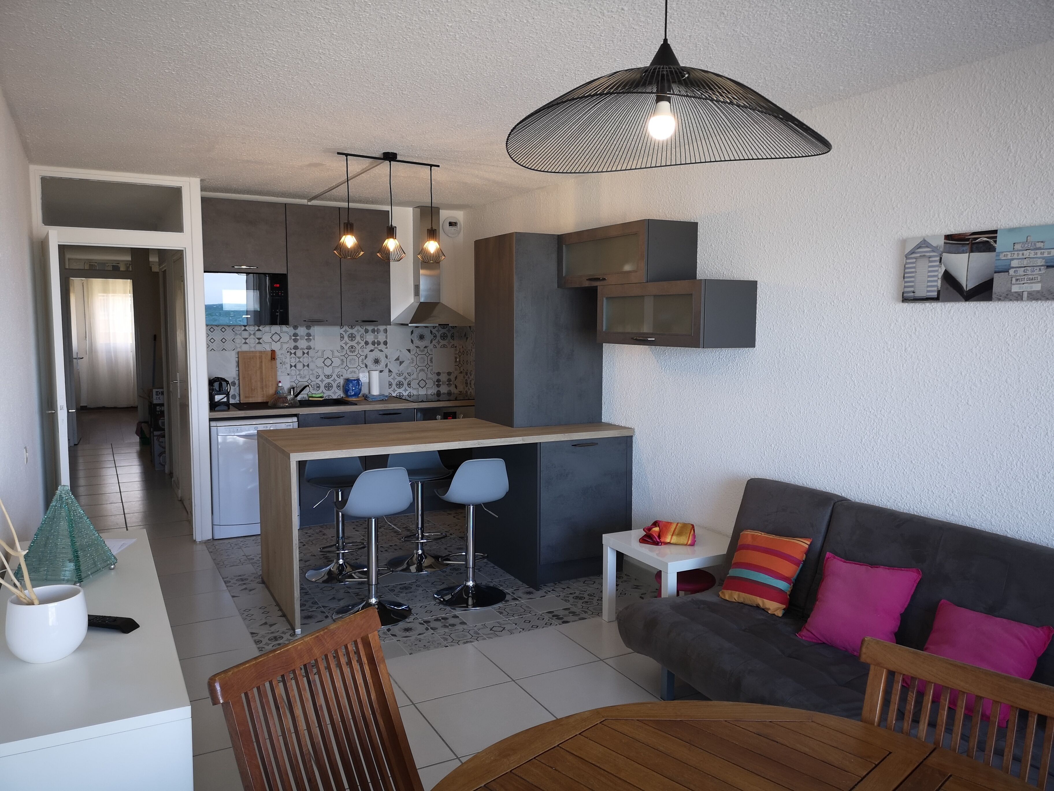 A modern kitchen with a central island, bar stools, and pendant lighting.