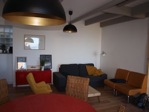 Una sala de estar moderna con un sofá, sillones, una mesa roja y una lámpara colgante grande.