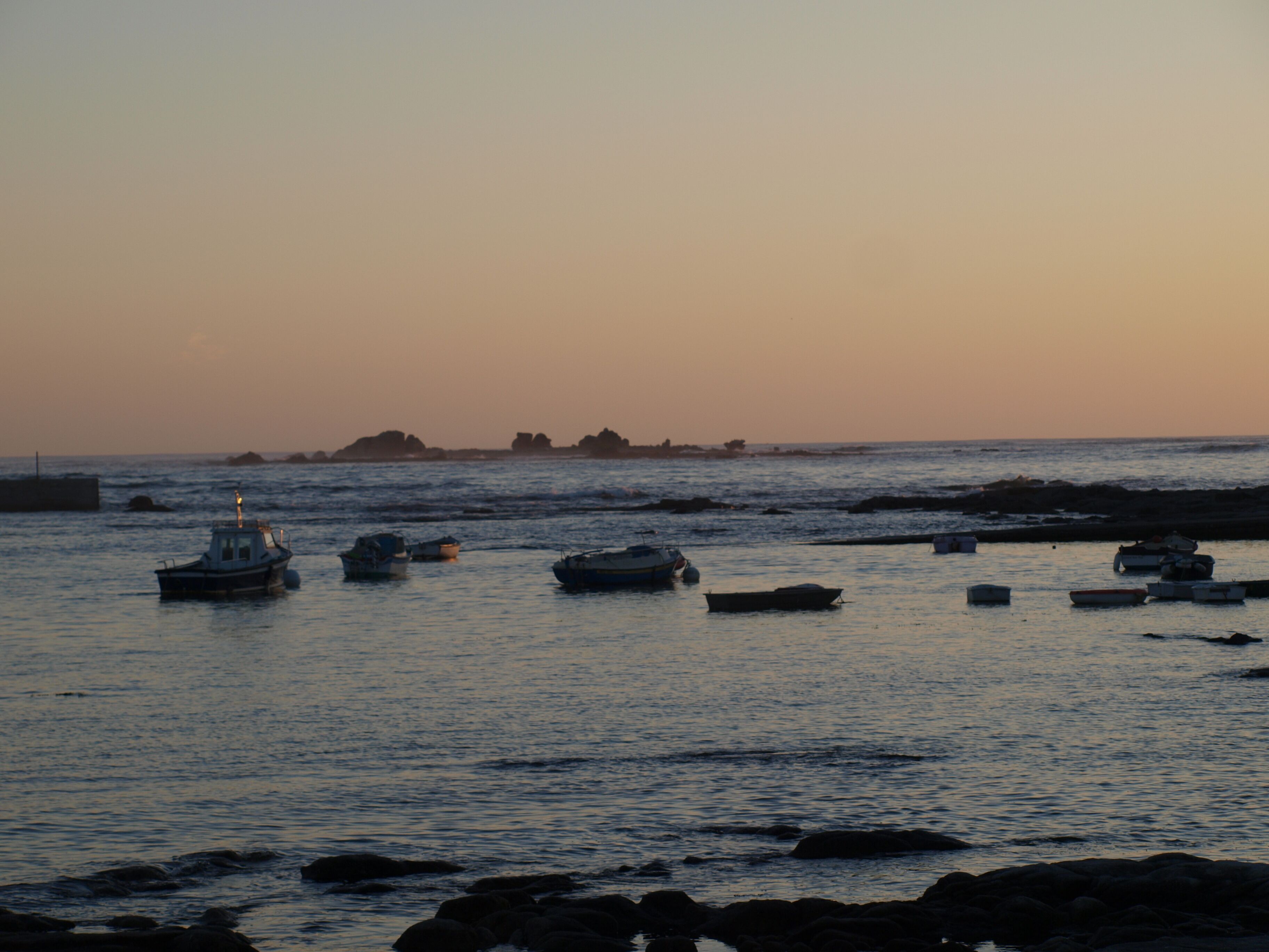 A coastal scene with boats anchored near rocky shores at sunset.