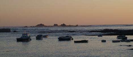 A coastal scene with boats anchored near rocky shores at sunset.