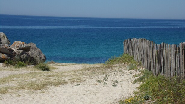 Une plage de sable avec une clôture en bois et des rochers.
