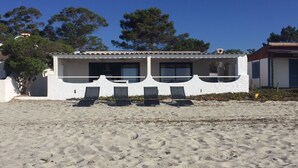 A beachside building with a white exterior, multiple windows, and a balcony with four lounge chairs. - T4 feet in water  (Ghisonaccia)