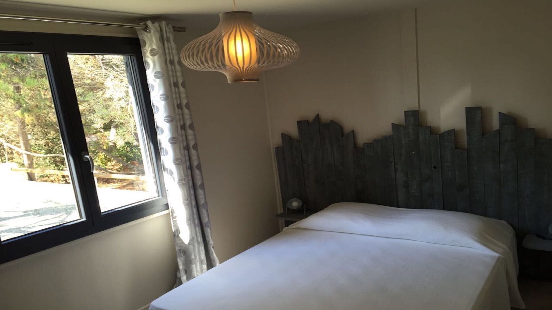 A bedroom with a bed, a window with curtains, and a unique wall decoration.