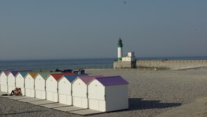 Une plage bordée d’une rangée de cabanes colorées et, au loin, un phare.