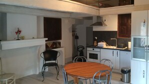 Een compacte keuken met een eethoek, met een houten tafel en metalen stoelen, een hangende lamp en een inbouwoven.