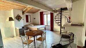 Een ruime woonkamer met houten vloer, een eettafel met stoelen, een trap en uitzicht op de omgeving door een raam.