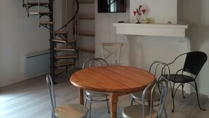 Een eetgedeelte met een houten tafel, metalen stoelen, een spiltrap en een witte toonbank met een flatscreen televisie.