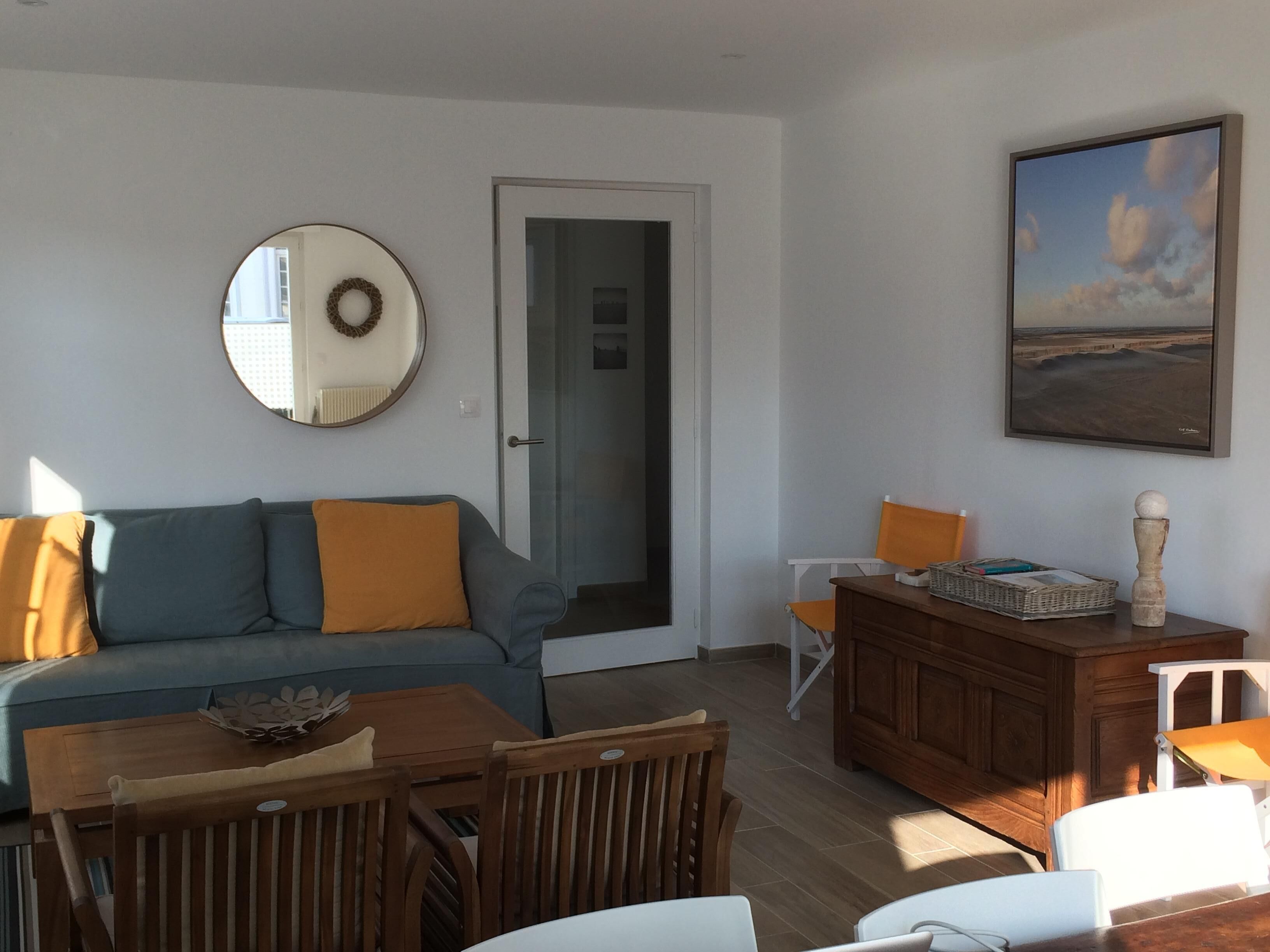 Een woonkamer met een bank, eettafel, stoelen, een houten kast, een spiegel en een lijst met een afbeelding aan de muur.