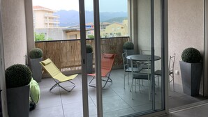Un balcón con puerta de vidrio, una mesa redonda y dos sillas.