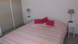 Un dormitorio con una colcha a rayas, dos lámparas de noche y dos almohadas rosas.