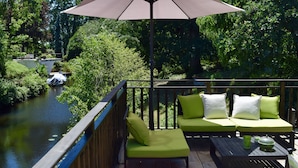 Una terraza con un sofá verde y una mesa, con vista a un río y una lancha.