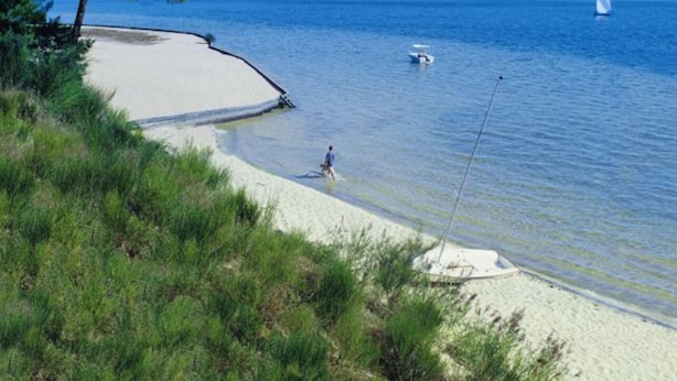 Una playa con aguas cristalinas, una orilla arenosa y una persona pescando.